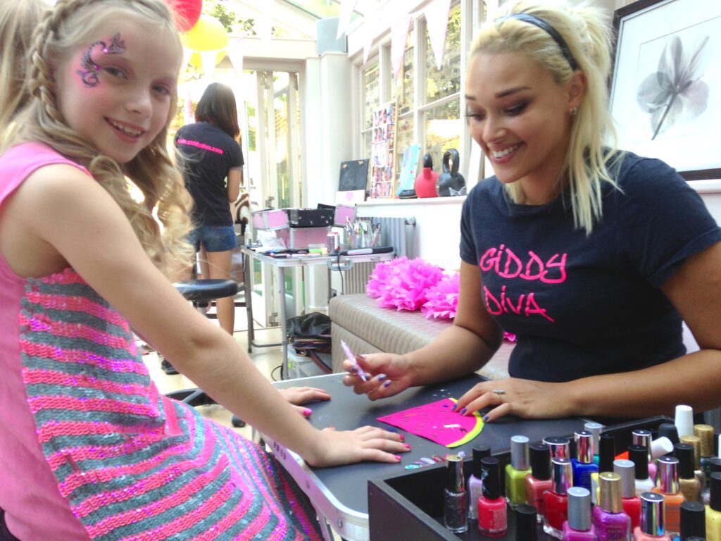 Two people sat opposite on a table. A young birthday girl is having her nails painted.