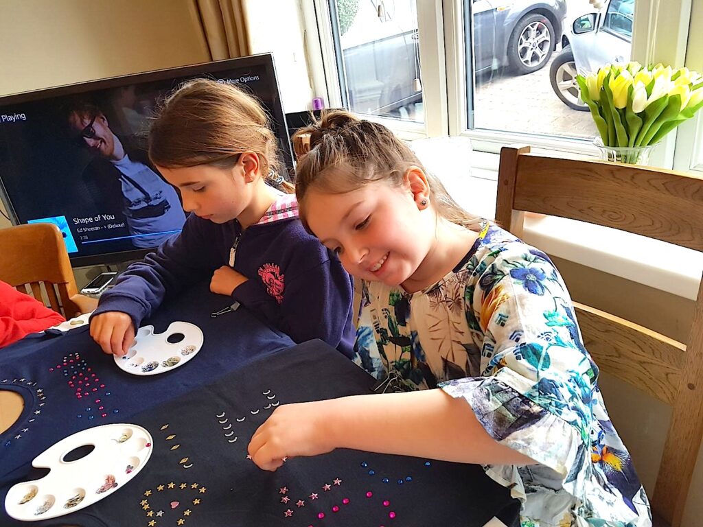 Two girls sat at a table decorating their fashion t-shirts.