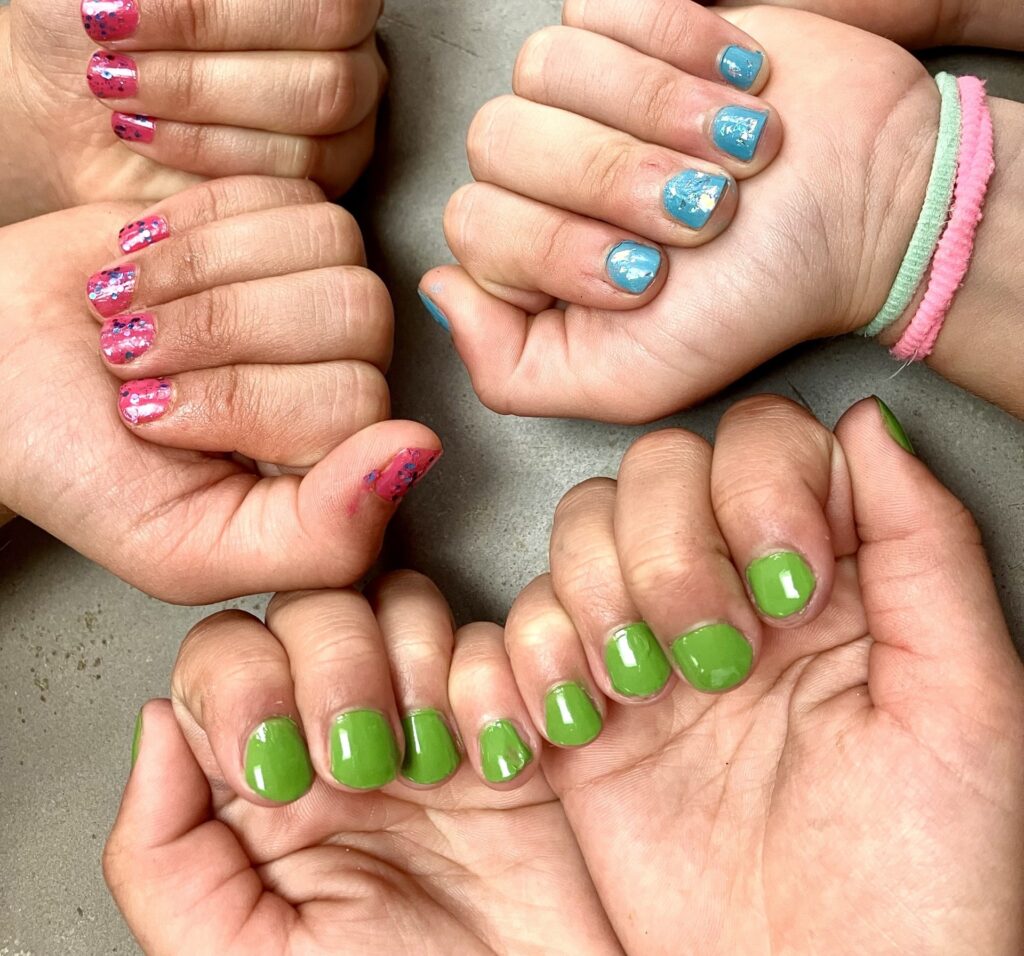 Three pairs of hands folding their fingers into the palm of theirs hands displaying the brightly coloured nail polishes painted on their nails.