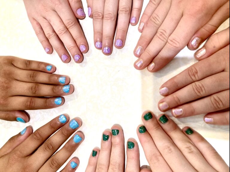 Four pairs of hands making the shape of a circle, they are showing off their brightly coloured polished nails.