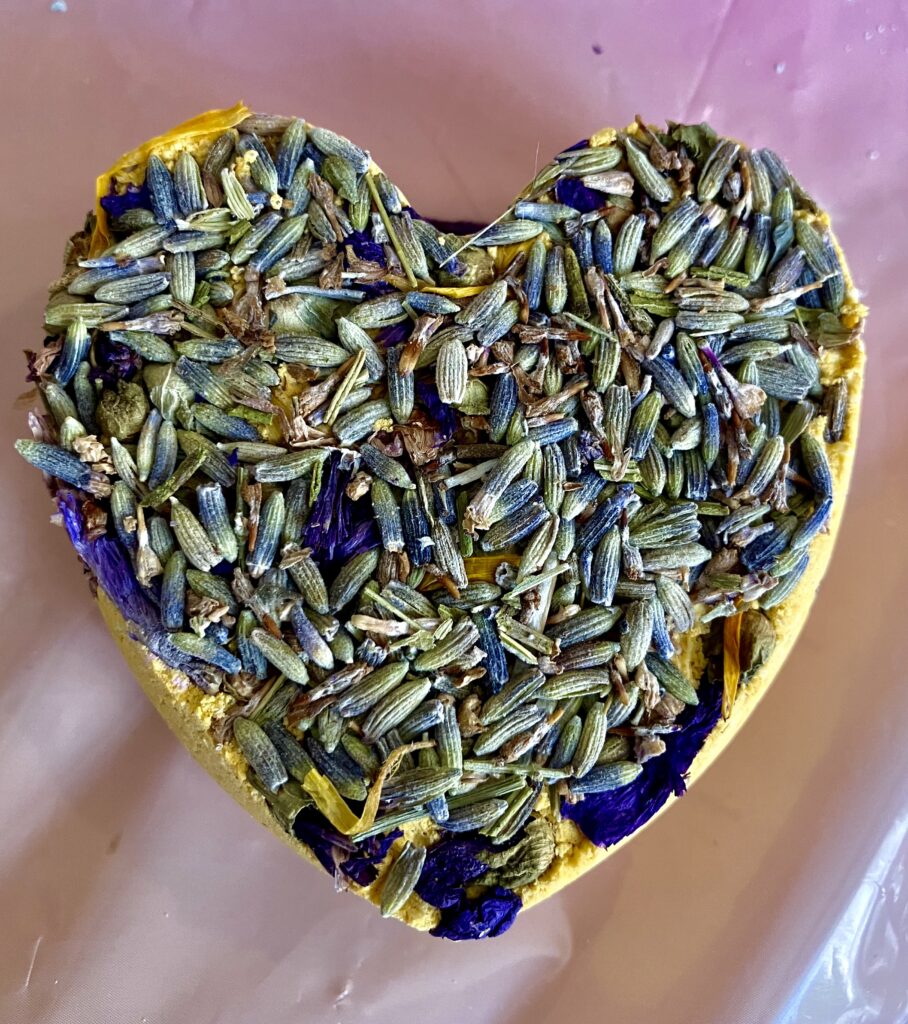 Yellow heart shaped bath-bomb with dried lavender and mallow flowers.