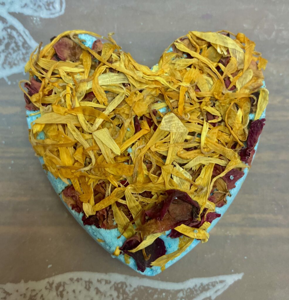 Blue heart shaped bath-bomb with dried marigold & rose flowers on top.