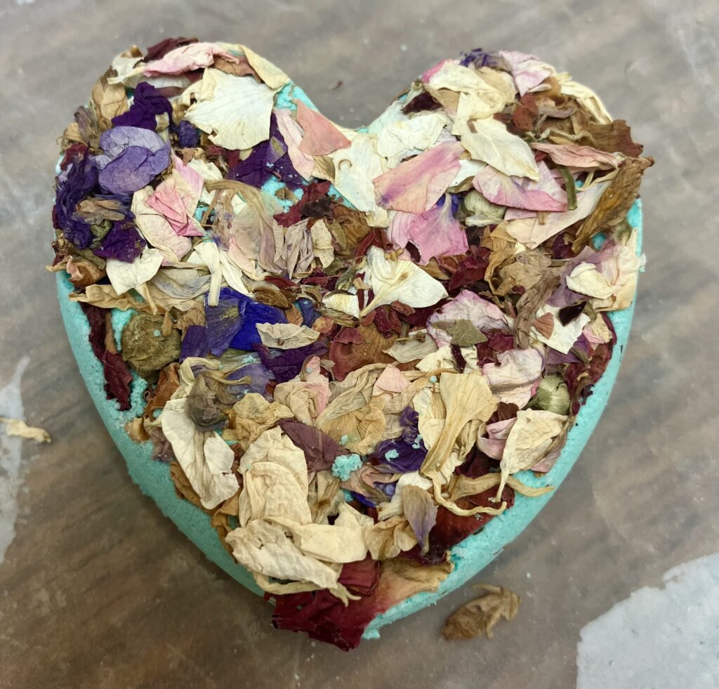 Light blue heart shaped bath-bomb with dried larkspur flowers.