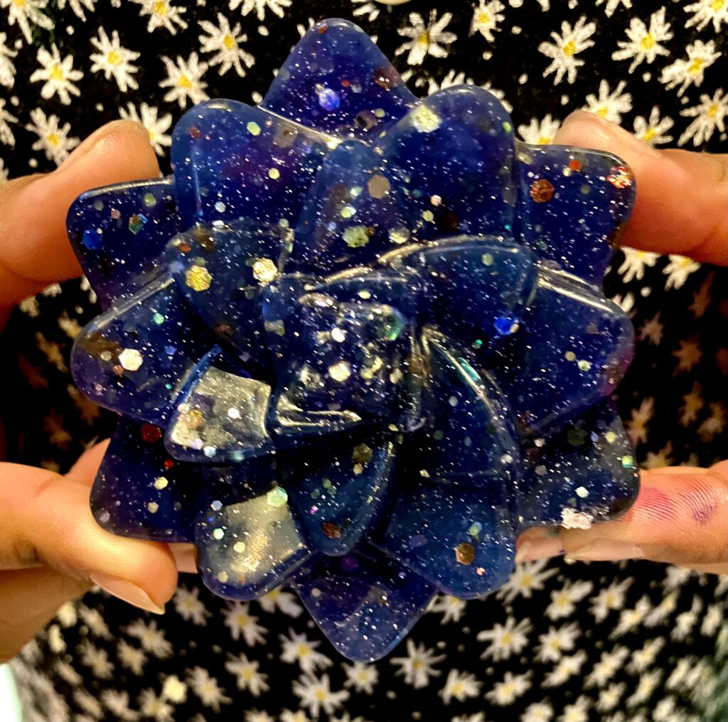 girl holding a soap that is shaped like a flower and glittery blue in colour.