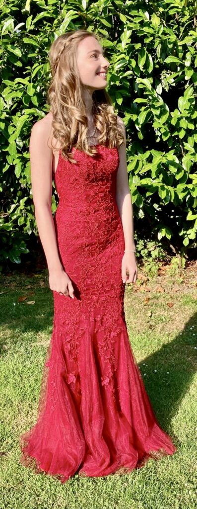 Full length photo of a girls in a red dress with hair and make up done ready to go to prom.