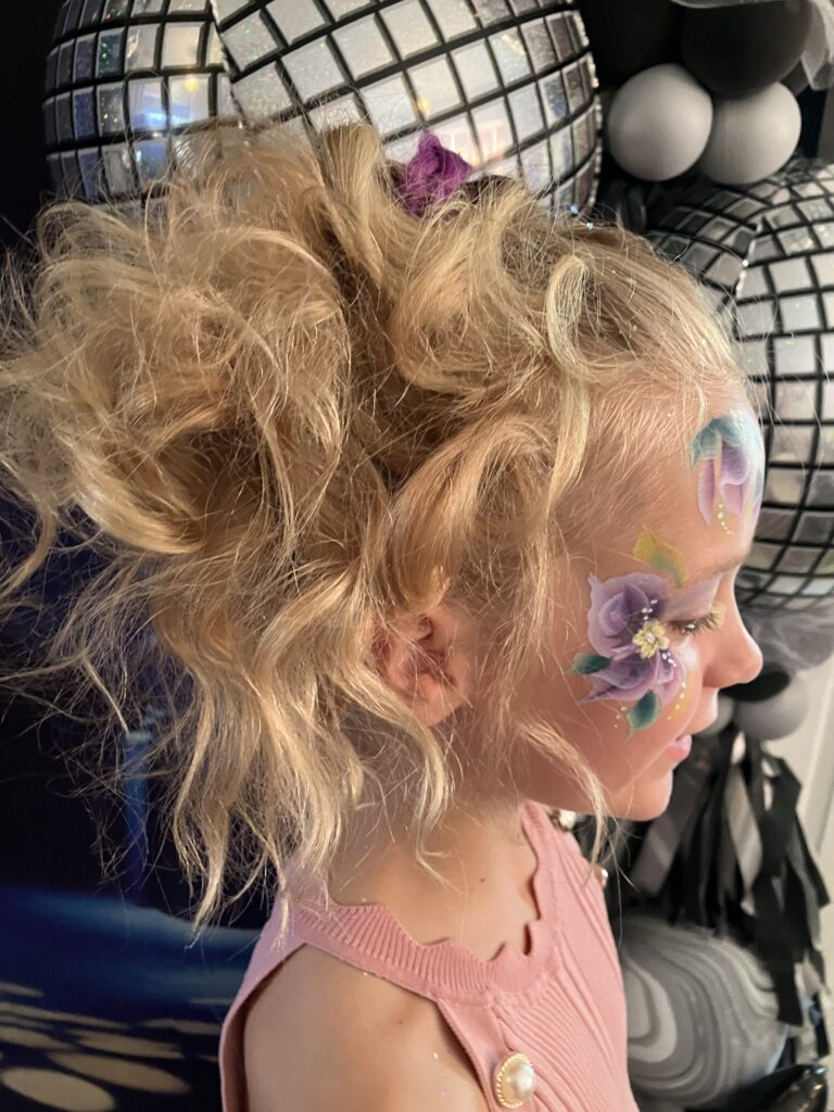 Girls with blonde hair gathered in a high up do and curled.