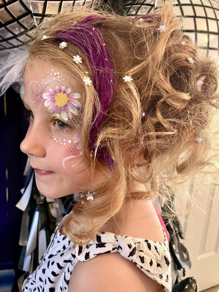 Girls with party hair, coloured purple hair extention and face art flower above her eye.
