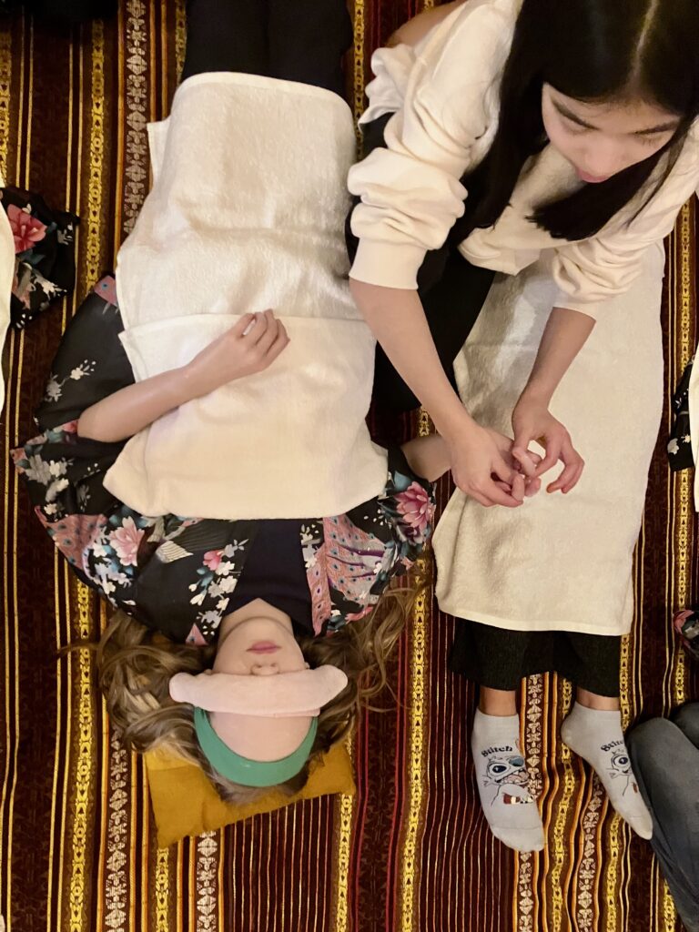 Girl lying down wearing a pink eye mask receiving a hand massage.