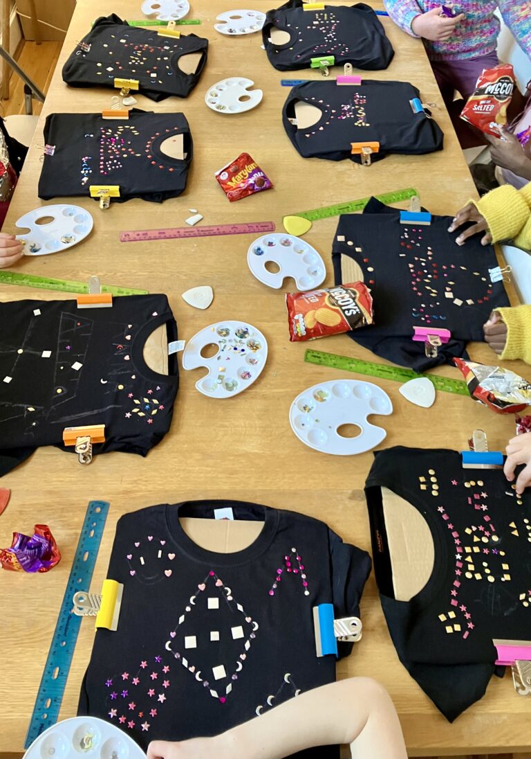 Six black t-shirts laid our on a table being decorated with rhinestone gems and embellishments.