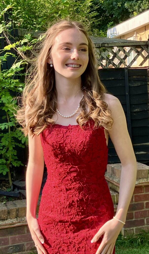 prom girl in red dress posing for a picture outside in the garden.